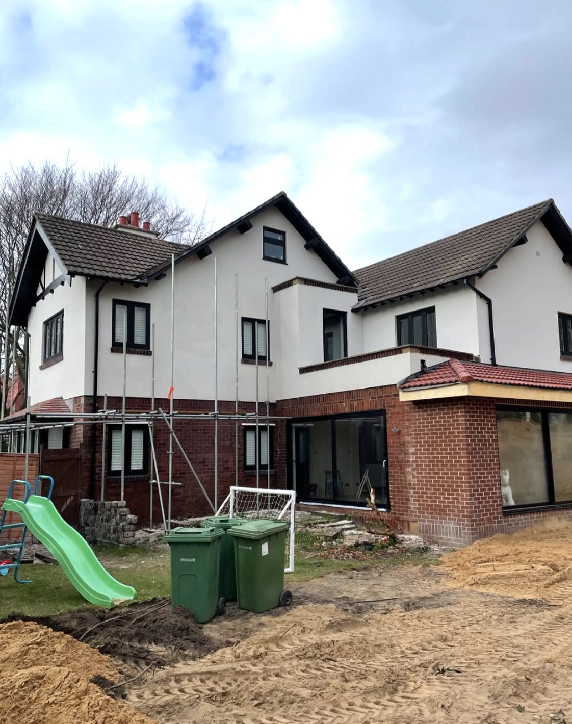Back of a large house partly rendered, with scaffold over a brick extension