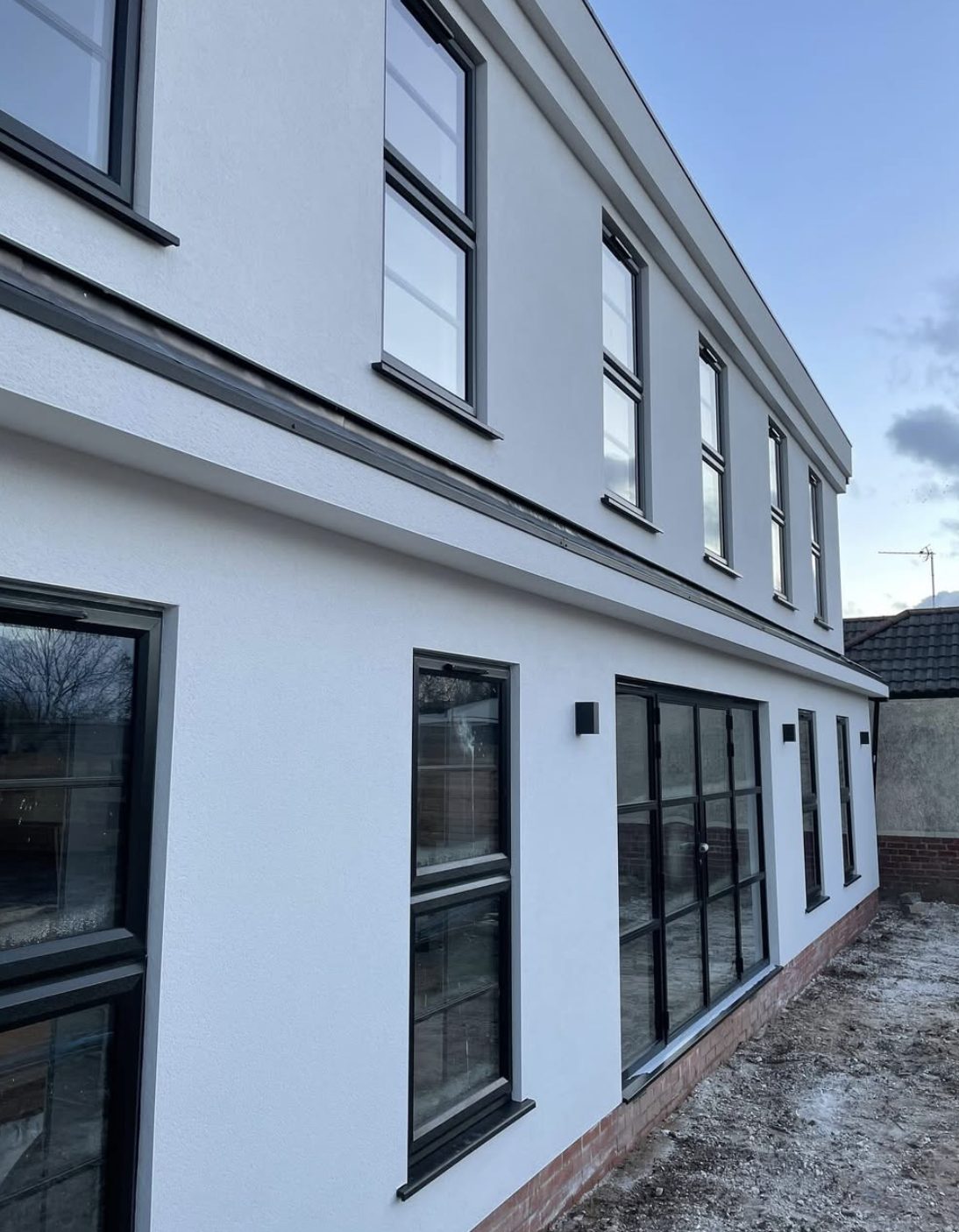 Long side wall in white render with a dark band course and black windows