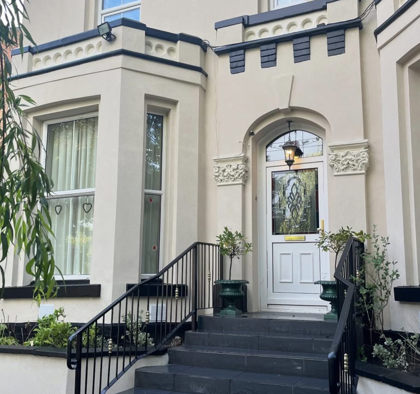 Victorian bay front in cream render with an ornate door surround and railings
