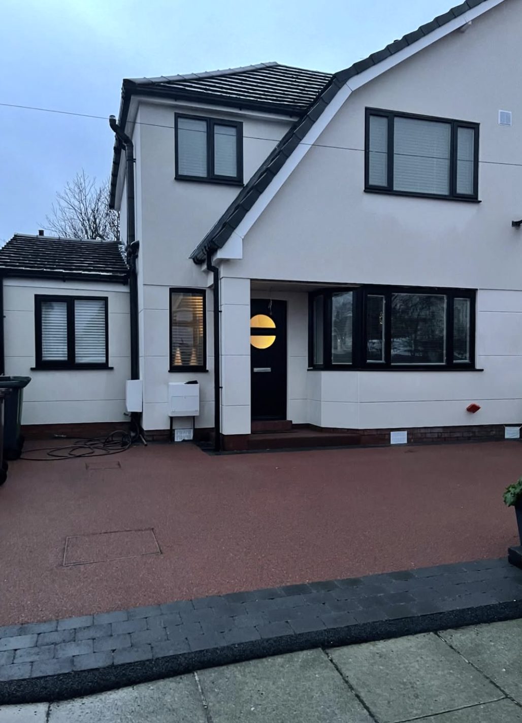 House in white render with anthracite window frames and a red paved drive